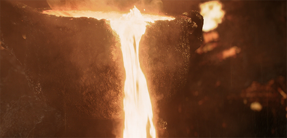 Glowing orange molten metal pours from a dark, textured crucible in a dark industrial setting.