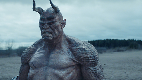 A muscular, grey-skinned humanoid creature with large horns and pointed ears against a cloudy sky.