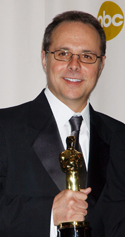 A smiling man in a black tuxedo and glasses holds a gold Oscar award.