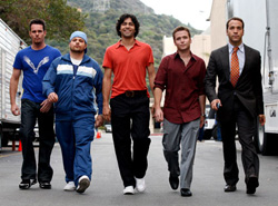Five men in casual and business attire walking toward the camera on a paved surface.