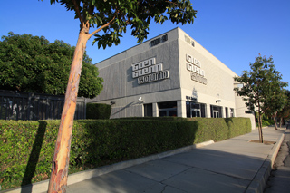 A large grey commercial building with Glen Glenn Sound signage behind a green hedge and a tree.