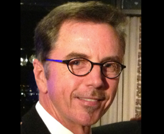 A man with short brown hair and black-rimmed glasses smiling at the camera.