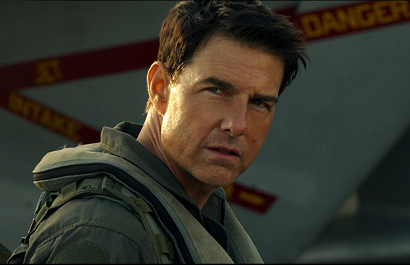 A man in a green flight suit looks intensely to the side in front of a jet.