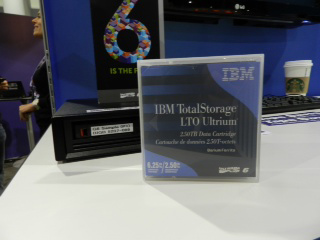 IBM TotalStorage LTO Ultrium 2.50TB data cartridge in its plastic case, next to a tape drive.
