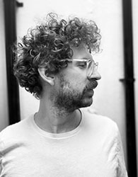 Black and white profile portrait of a man with curly hair and glasses looking to the side.