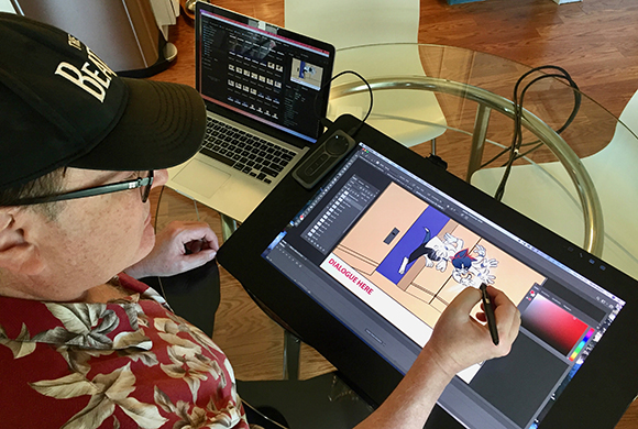 An artist uses a stylus on a large digital drawing tablet connected to a laptop on a glass table.