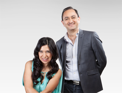 A smiling man in a grey suit and a woman in a teal top posing together against a light grey background.