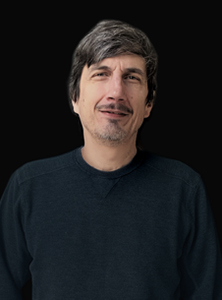 A man with dark, salt-and-pepper hair and a goatee wearing a dark crewneck sweater.
