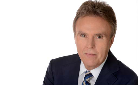 A man with light brown hair wearing a dark blue suit, white shirt, and striped tie.