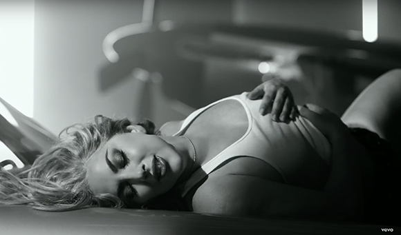 Black and white close-up of a woman lying down with her eyes closed and hand on her chest.