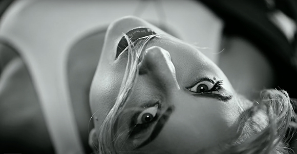 Black and white close-up of a person's face tilted upside down with dramatic eye makeup.