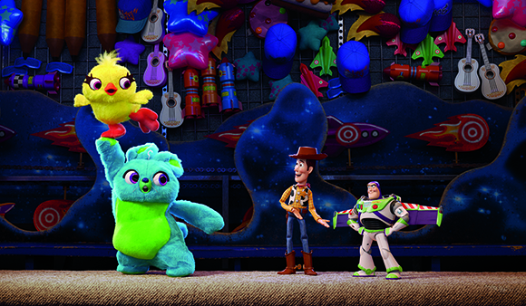 Buzz Lightyear, Woody, a large blue plush, and a small yellow chick toy stand before a carnival game.