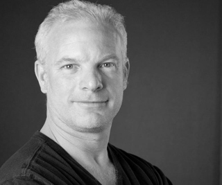 Black and white headshot of a middle-aged man with short light hair looking at the camera.