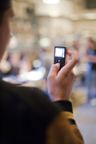 A person holds up a small black digital device with a glowing screen in a blurred indoor setting.