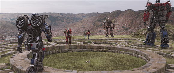 Large mechanical robots stand in a stone circle within a vast, hilly landscape.