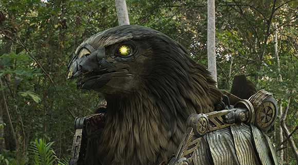 A large, brown, mechanical bird creature with a glowing yellow eye in a dense forest.