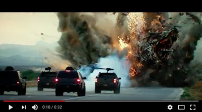 A massive explosion with debris and smoke rises behind four black SUVs driving on a road.
