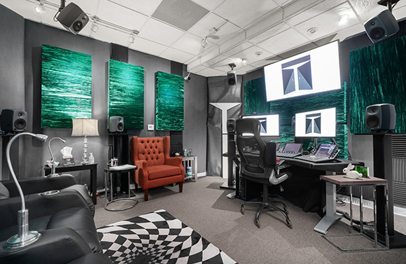 A professional recording studio with green acoustic panels, a mixing desk, and black studio monitors.