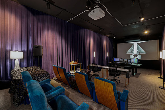 A dark home theater with blue velvet chairs, purple curtains, and a large projection screen.