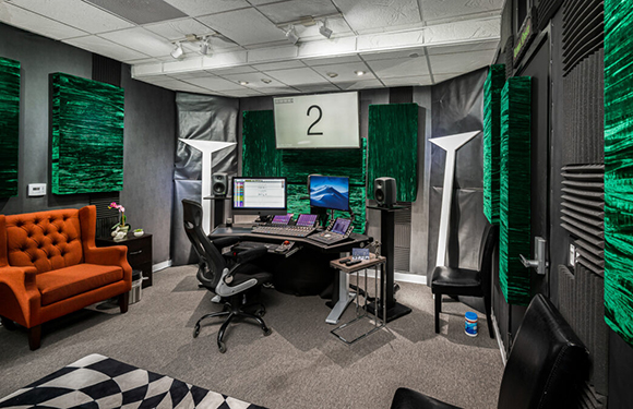 A professional recording studio with green acoustic panels, a mixing desk, and computer monitors.