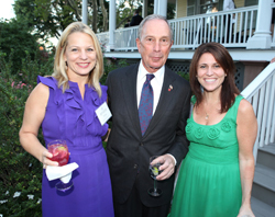 A woman in purple, a man in a dark suit, and a woman in green posing together outdoors.