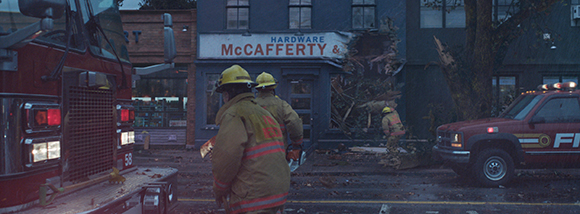 Firefighters stand near a red fire truck in front of a damaged McCafferty Hardware building.