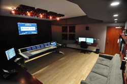 A professional recording studio featuring a large mixing console, computer workstations, and a grey sofa.