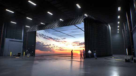 A massive digital screen showing a sunset landscape inside a dark, cavernous industrial space with people standing before it.