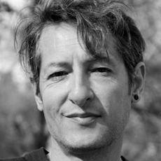 Black and white close-up portrait of a person with wavy hair smiling slightly.