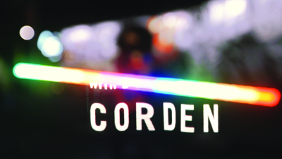 A blurred background with a bright, multicolored horizontal neon light bar above the word CORDEN in white.