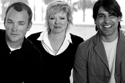 Black and white portrait of three smiling adults standing side by side outdoors.