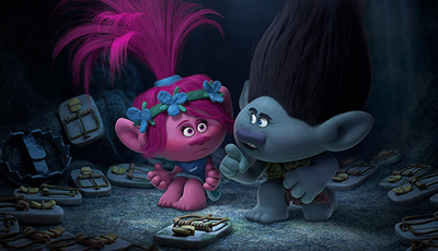A pink troll with blue flowers and a grey troll with dark hair look worried in a dark cave.
