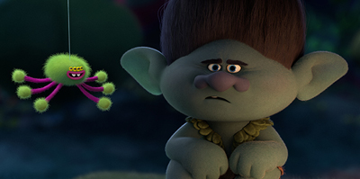 A grey troll with brown hair looks skeptically at a small, fuzzy green spider toy hanging by a string.