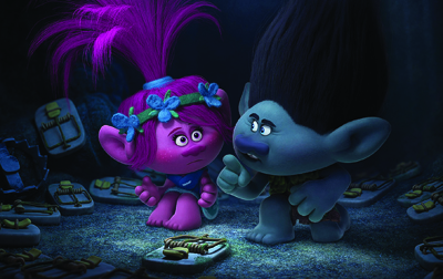 A pink troll with blue flower hair accessories and a grey troll look at each other in a dark cave.