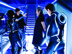 Four people in a blue-lit futuristic corridor wearing black suits with glowing blue accents.