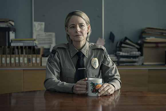 A female police officer in uniform sits at a wooden table with a mug in an office.