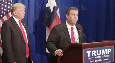 Donald Trump stands behind Chris Christie as Christie speaks at a podium with a Trump campaign sign.
