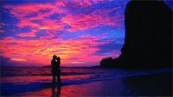 Silhouette of a couple embracing on a beach under a dramatic pink and purple sunset sky.