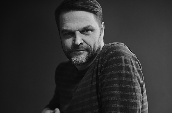 Black and white portrait of a man with a beard wearing a striped shirt looking toward the camera.