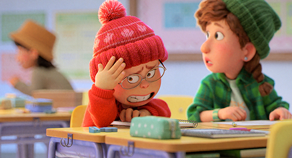 An animated girl in a red beanie looks distressed at her desk while another girl in a green beanie watches her.