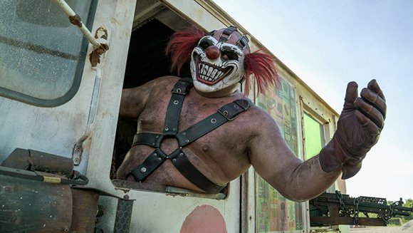 A person wearing a menacing clown mask and black leather harness leans out of a white van window.