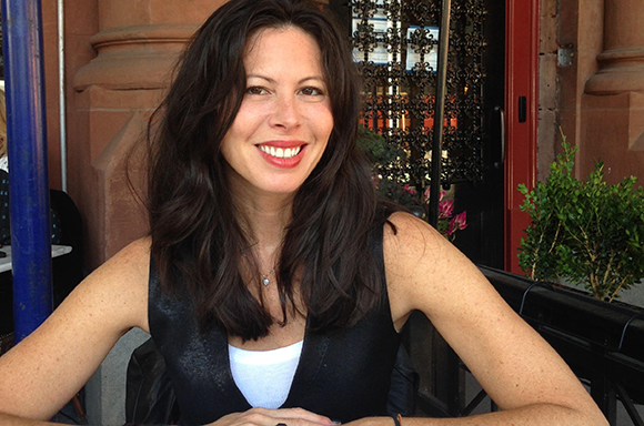 A smiling woman with long dark hair wearing a black vest over a white top.