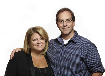 A man in a blue checkered shirt with his arm around a woman in a black blazer.
