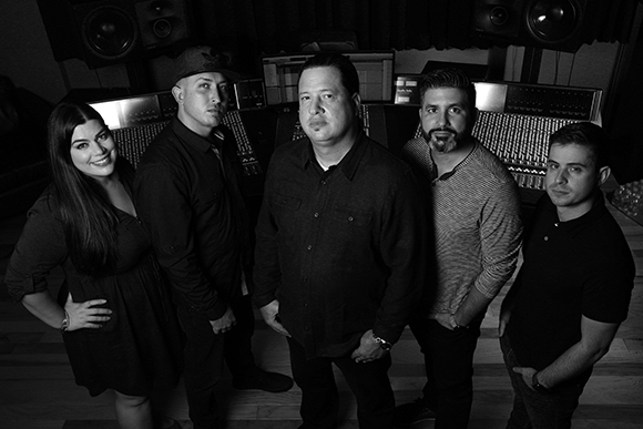 Five people, three men and two women, posing together in a dark studio.