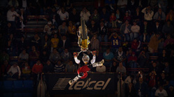A gymnast in a white and red uniform performs a mid-air flip before a dark crowd.