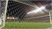 A view through a soccer net looking out onto a green field in a stadium under bright lights.