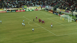 Soccer players on a green field during a match with a large crowd in the stadium stands.