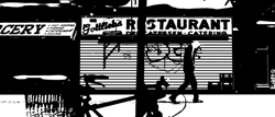 High-contrast silhouette of a person walking past a closed restaurant with graffiti on its metal shutters.