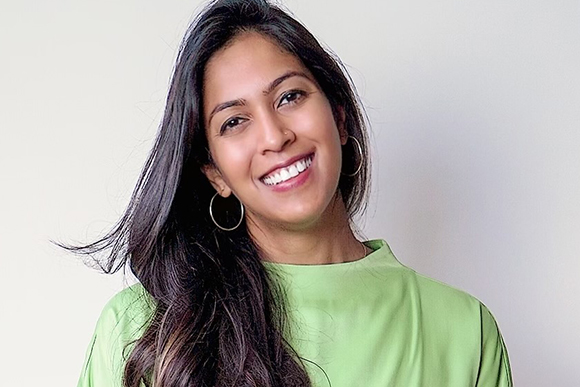 A smiling woman with long dark hair and silver hoop earrings wearing a lime green top.