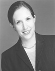 A smiling woman with dark hair pulled back, wearing a dark blazer and a necklace.